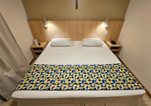 a bedroom with a large bed with a yellow and blue blanket at Hotel Rainha dos Apóstolos in Aparecida