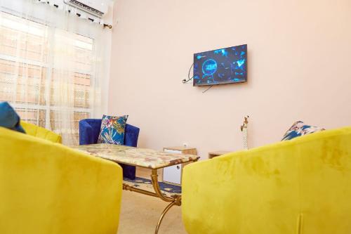 a living room with yellow chairs and a table and a tv at Cosy Refuge in Bonabéri