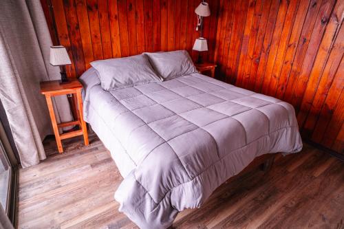 a bed in a room with wooden walls and wood floors at Cabañas El Bosque in Maitencillo