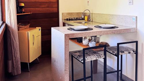 a kitchen with a counter with two stools and a sink at Sítio Balango: Seu refúgio em Domingos Martins. Chalés para casais e casa para grupo de pessoas in Domingos Martins