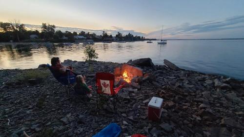 a woman and child sitting around a campfire on a lake at Loza house coastal design unit with lake & mountain views in Plattsburgh