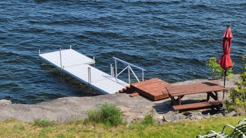 a dock with a picnic table and an umbrella on the water at Loza house coastal design unit with lake & mountain views in Plattsburgh