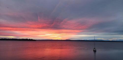a boat in the middle of a lake with a sunset at Loza house coastal design unit with lake & mountain views in Plattsburgh