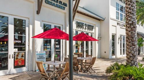 two tables with red umbrellas in front of a store at Mistral 10 in Seacrest