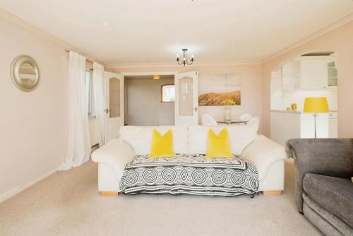 a living room with a white couch and yellow pillows at Stylish apartment - 2 min walk from Ogmore by sea beach with private garden, sea views & stunning sunsets, dog friendly in Tythegston