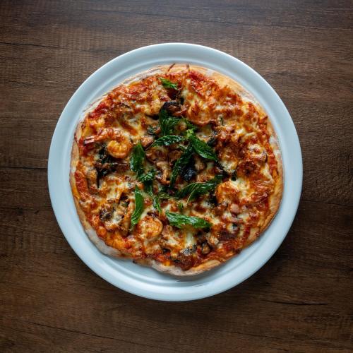 a pizza on a white plate on a wooden table at The Skye Phnom Penh Hotel & Apartments in Phnom Penh