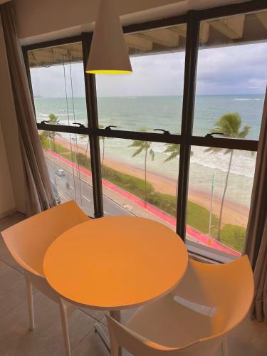 a table and chairs in front of a window with the beach at Refúgio do Mar 703 - Condomínio Edifício Ritz Suítes Home Service in Maceió