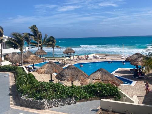 a swimming pool with straw umbrellas and the ocean at Lagoon Sunset view entire apartment in Cancún