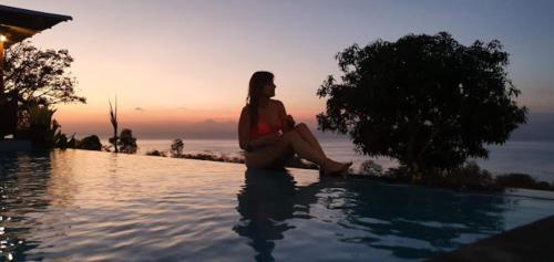 a woman sitting on the edge of a swimming pool at Bataran Garden Cottage in Nusa Penida