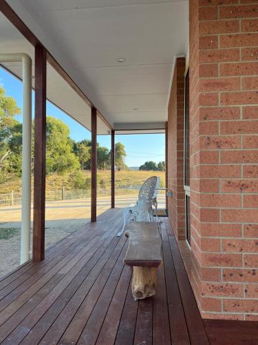 a bench sitting on a wooden porch with a brick wall at Two bedrooms Escape to Countryside Retreat in Wamboin