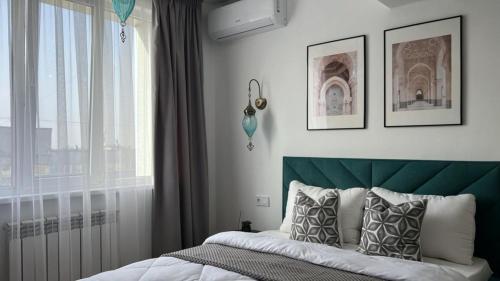 1 dormitorio con 1 cama con cabecero verde y ventana en Eastern style apartment in Golden Square!, en Almaty