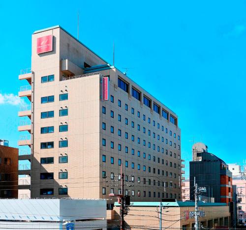 a tall building with a red sign on it at Nest Hotel Matsuyama in Matsuyama