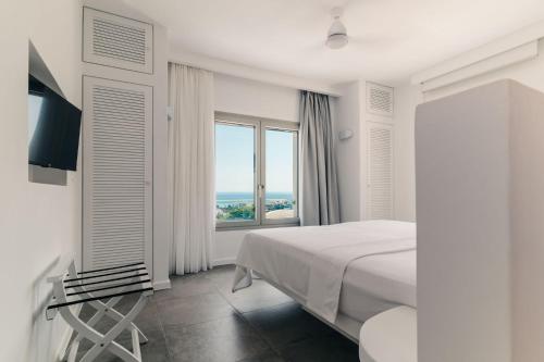 a white bedroom with a bed and a large window at Makrikythera Luxury Suites - Private Pool or Hot Tub Suites in Dhiakofti