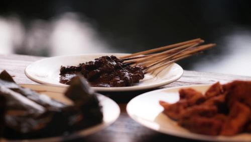 two plates of food on a wooden table with chopsticks at Kubu Damai Guest House in Jatiluwih