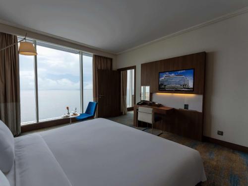 a hotel room with a large bed and a desk and window at Novotel Jazan in Jazan