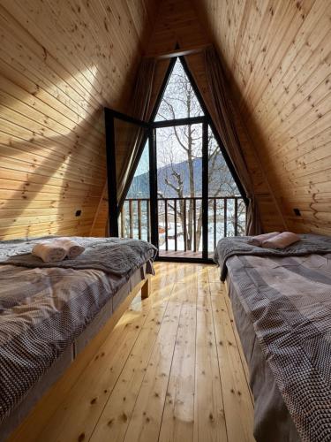 two beds in a room with a large window at Cozy Cottage JuFu in Mestia