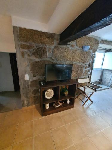 a living room with a tv and a stone wall at Casa do Tinte - Gouveia-Folgosinho in Vila Cortês da Serra