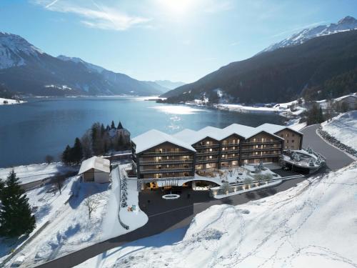 a lodge in the snow next to a body of water at DAS GERSTL Family Retreat in Resia