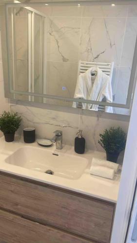 La salle de bains est pourvue d'un lavabo, d'un miroir et d'un peignoir blanc. dans l'établissement 4 Bedroom Apartment - Near docks and metro, à Rouen