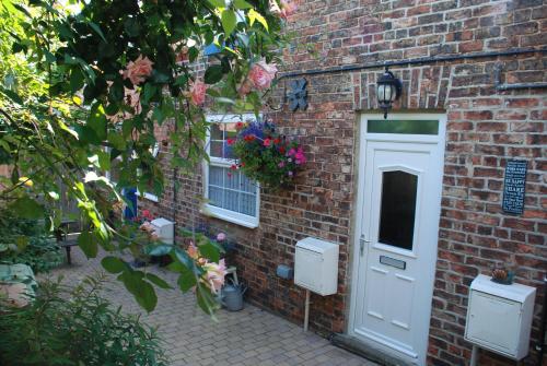 a brick building with a white door and flowers at Saltburn Holidays Bluebell Cottage in Guisborough