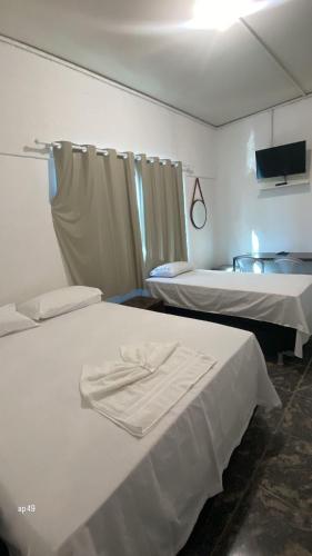 a room with two beds with white sheets and a tv at Hotel Pousada Do Sol II in Aragarças