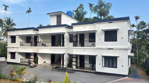 a white building with palm trees in the background at VENUE DAYS homestays in Meenangadi