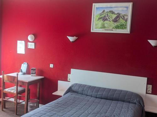 a bedroom with a red wall with a bed and a desk at Hôtel Le Rider in Bort-les-Orgues
