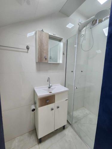 a white bathroom with a sink and a shower at Apartamento-3 pé na areia, churrasqueira, acesso a lagoa, vista para rio, Torres e serra gaúcha in Passo de Torres