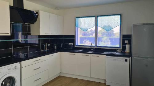 une cuisine avec des armoires blanches, un évier et une fenêtre dans l'établissement LOCATION SAISONNIERE PRES DE LA MER avec ROOFTOP, à Riantec