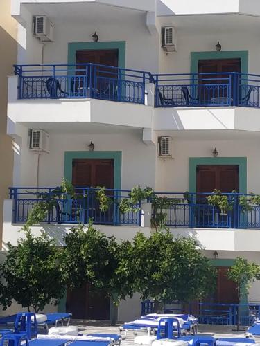 a tall white building with blue balconies and trees at George Studios Stalis in Stalida