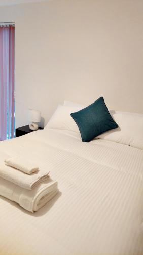 a white bed with a blue pillow and towels on it at Seaside Serenity in Swansea