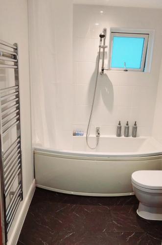 a white bathroom with a tub and a toilet at Seaside Serenity in Swansea