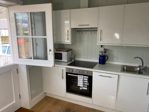 a white kitchen with white cabinets and a sink at NEW Cosy Gem, Near Beach, Log-Burner, Dog Friendly in East Wittering
