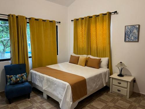 a bedroom with a bed with yellow curtains and a blue chair at Casa en río san Juan 4 habitaciones in Río San Juan