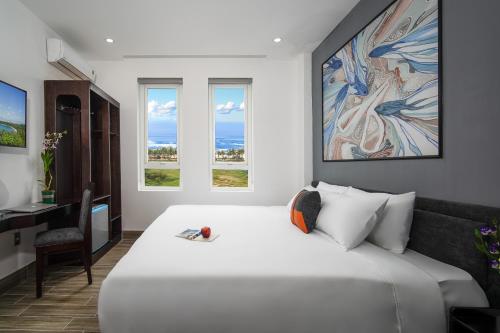a bedroom with a large white bed with a desk and windows at Coral Cove Hotel in Danang