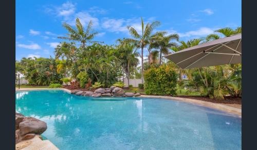 a swimming pool with an umbrella and palm trees at Strand Marina-Ground Floor with Courtyard in Townsville