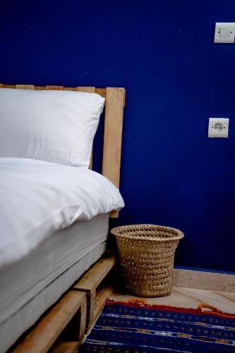 a bed with a blue wall and a basket next to it at Ossmon Surf House - Anza in Agadir