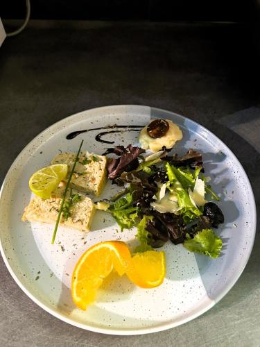 a plate of food with a salad and an orange slice at Gabrielle hôtel in Aiguines