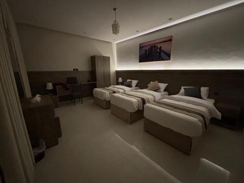 Una habitación de hotel con tres camas y un escritorio. en شقق زهرة السلام الفاخرة, en Medina