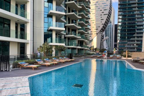 a swimming pool with lounge chairs and buildings at Simply Comfort Vacation Homes Rental in Missoni Top Floor with Sea, Canal and Burj Khalifa Views in Dubai