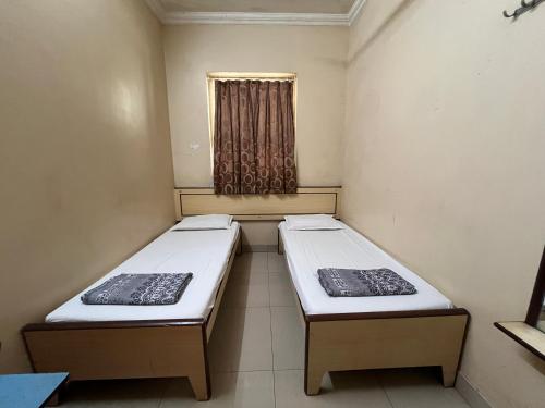 two beds in a small room with a window at Milan Guest House in Mumbai