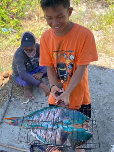 a young boy is cooking food on a grill at Riung Tiga Empat Tujuh Guesthouse in Riung