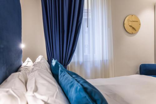 a bed with blue pillows next to a window with a clock at Opera Relais De Charme - Aparthotel in Verona