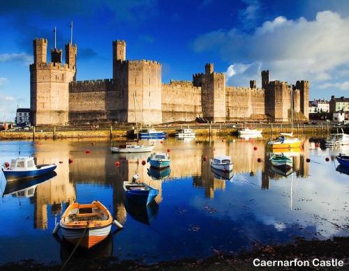 a castle with boats in the water in front of it at Lowern, Luxury Lodge with Hot Tub and Games Room in Menai Bridge