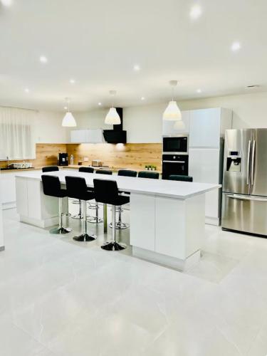 une cuisine blanche avec un comptoir blanc et des tabourets noirs dans l'établissement Villa 220 m2 avec 5 chambres 6 lits doubles 2 toilettes 2 salles de bain, à Beire-le-Châtel