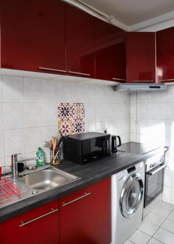 La cuisine est équipée de placards rouges, d'un évier et d'un four micro-ondes. dans l'établissement Le Petit Parisien, au Kremlin-Bicêtre
