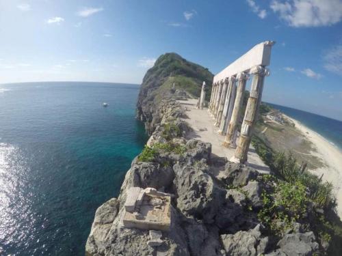 a building on a cliff next to the ocean at RedDoorz @ Sukitel Budget Hotel Nasugbu in Nasugbu