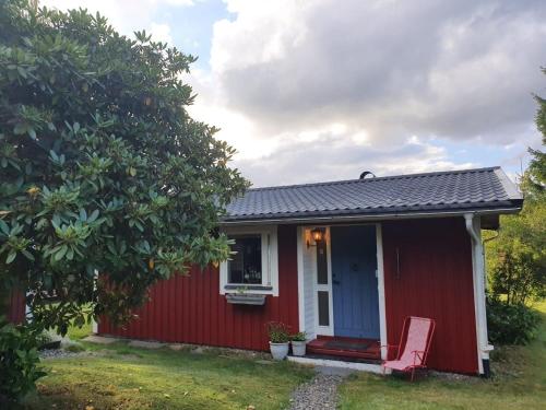 a red house with a red chair in a yard at Peaceful home in cozy cabin by the lake in Hyssna