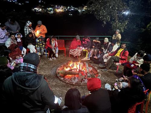 a group of people sitting around a fire at The Himalaya Retreat Resort, Experience Nature in the Lap of Himalayas in Mussoorie