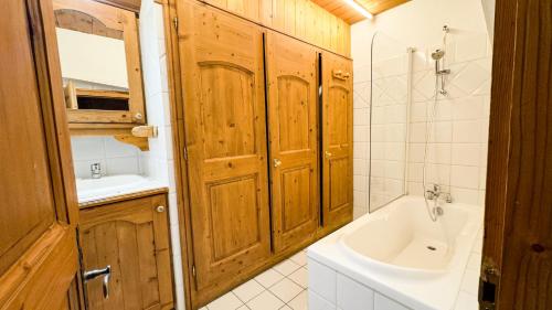 La salle de bains est pourvue d'armoires en bois, d'un lavabo et d'une baignoire. dans l'établissement Appartement Avec Sauna, à Chamonix-Mont-Blanc